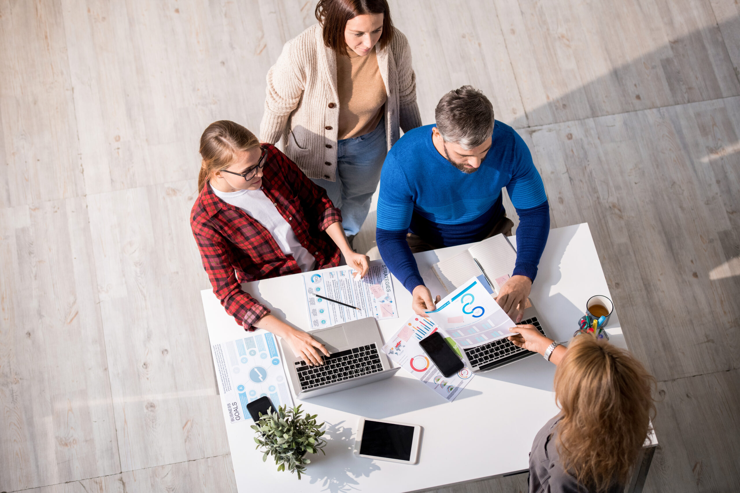 Creative team of marketing professionals working with charts in modern office: secretary giving paper to colleagues brainstorming about project